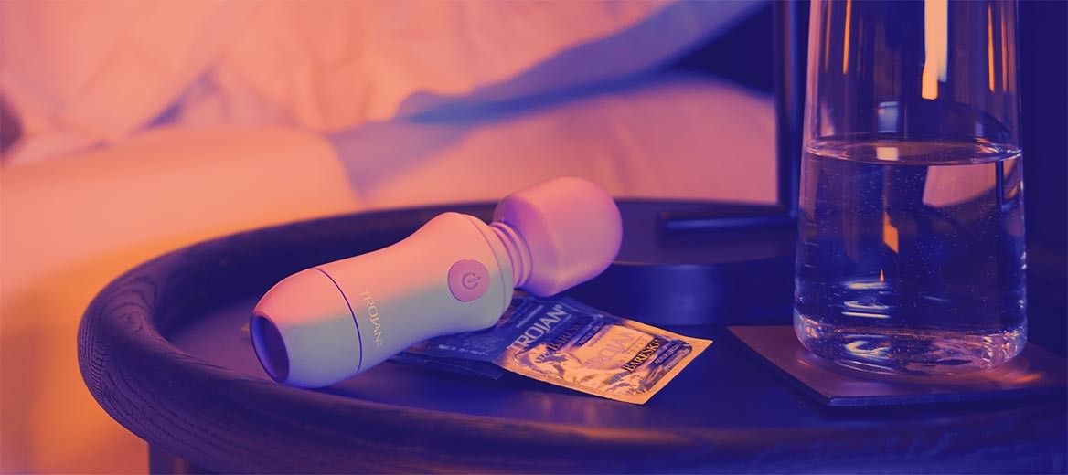 Trojan™ vibrator, condoms and glass of water on a bedside table.