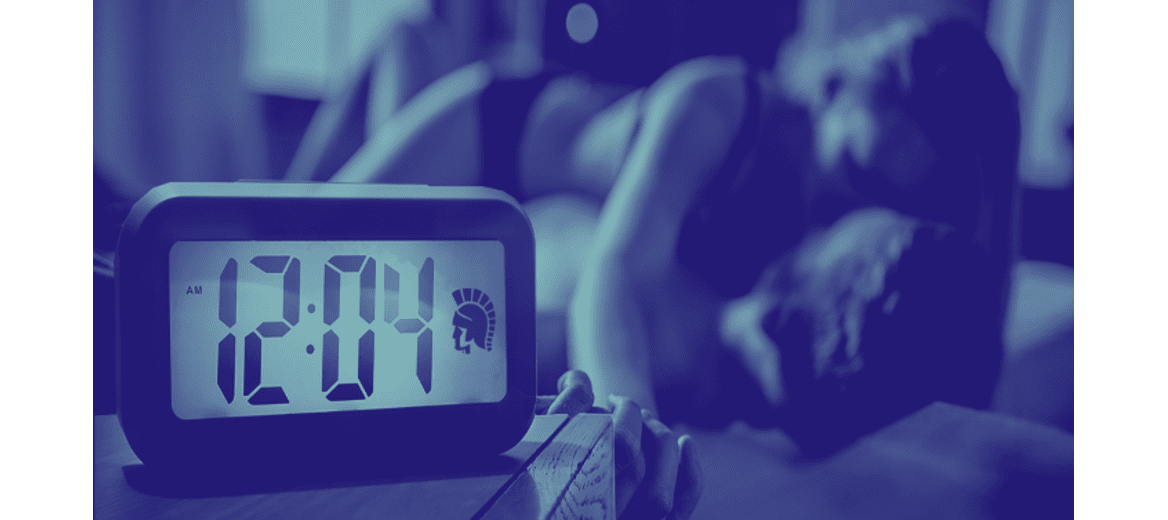 Alarm clock with Trojan logo shows the time while a man and woman kiss on a bed.